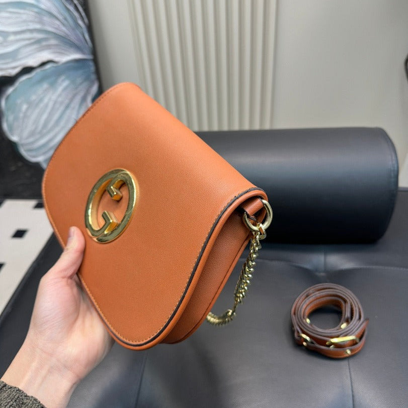Brown leather handbag with gold chain held by a hand on a black surface.