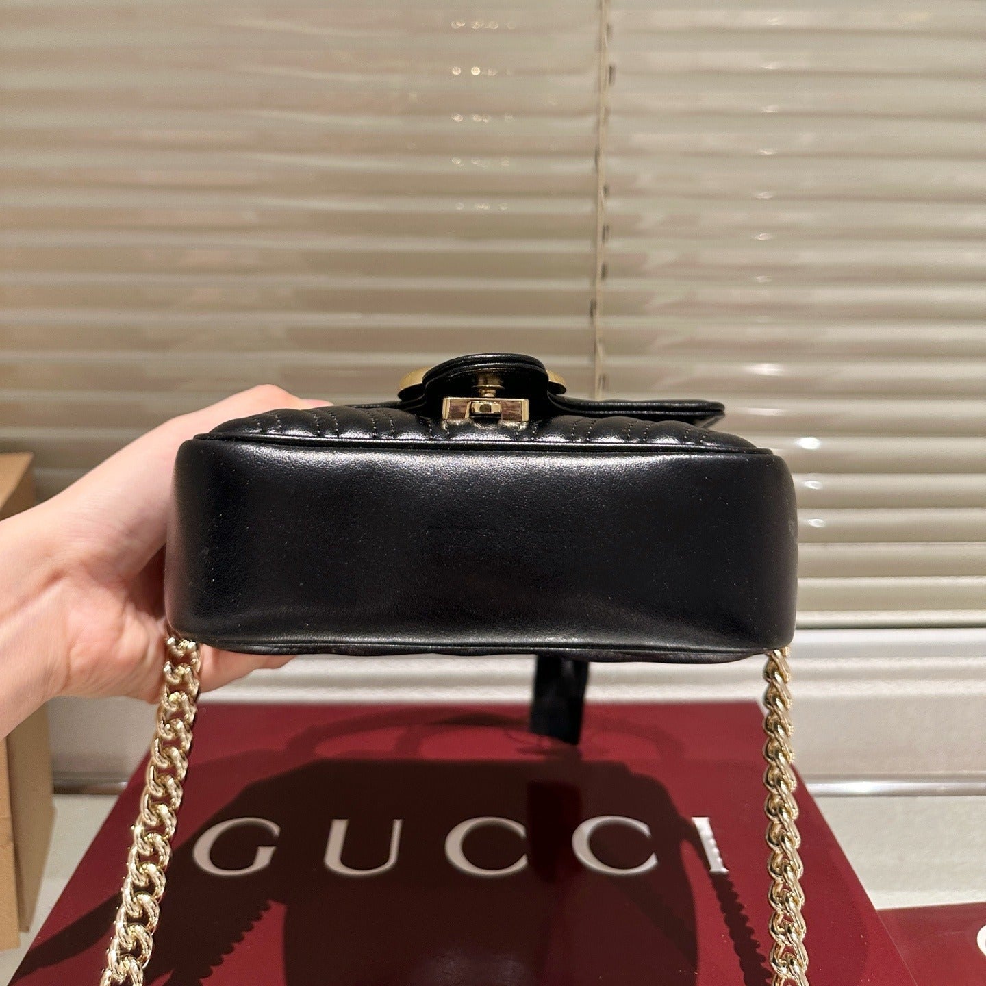 Black handbag with gold chain held by a hand on a Gucci branded surface.